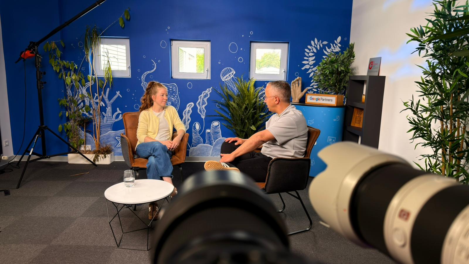 Hinter der Kamera während einer Deep-Dive-Aufnahme im AWEOS-Studio: Profikamera im Vordergrund, im Hintergrund läuft das moderierte Interview