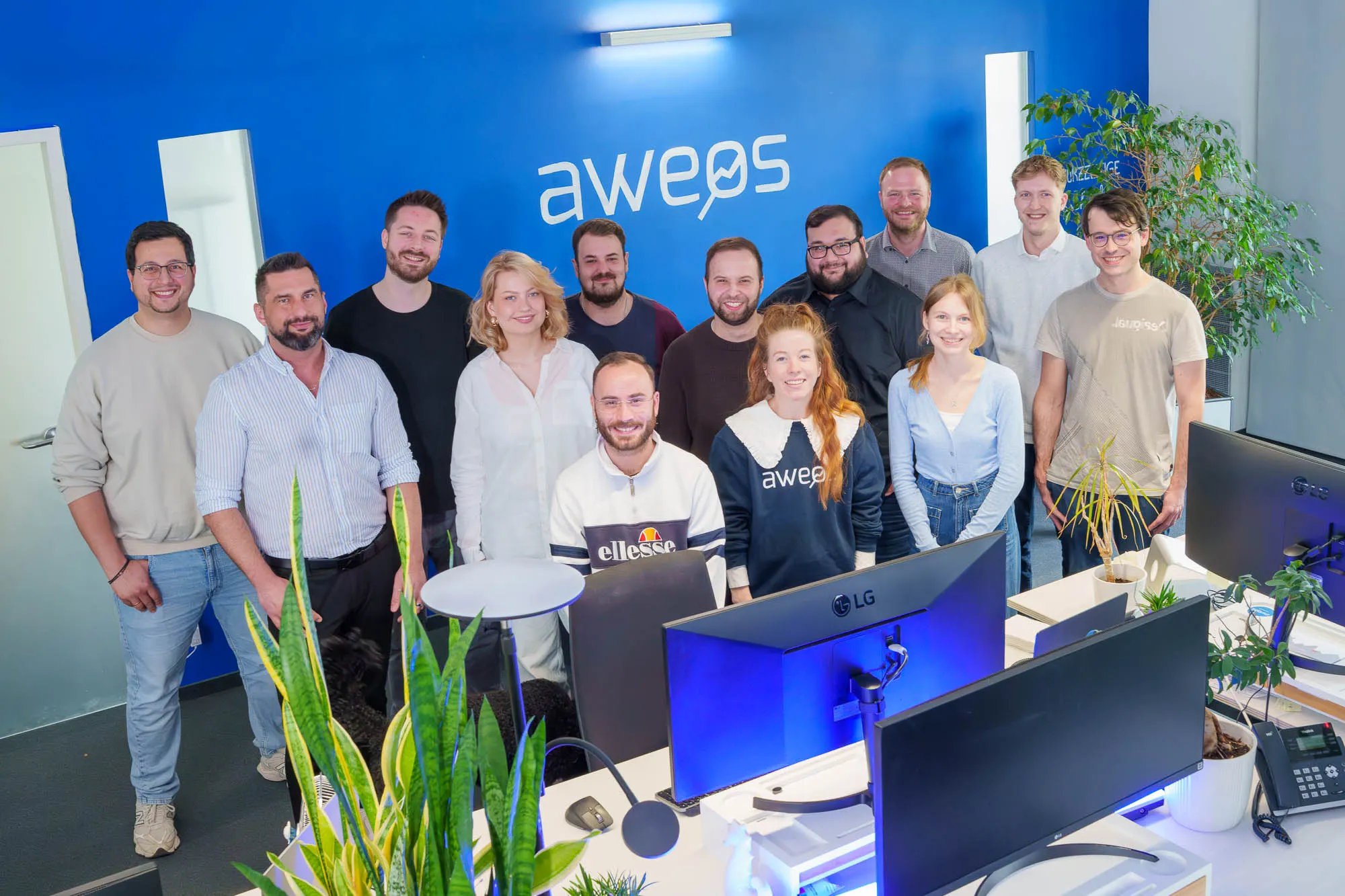 Das Team der Digitalagentur AWEOS aus Solingen im Büro vor dem AWEOS-Logo
